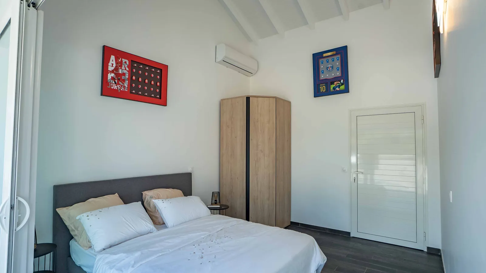 Chambre Sport — lit gris, armoire d'angle et vitrines de souvenirs sportifs, villa House of Harmony, Goyave