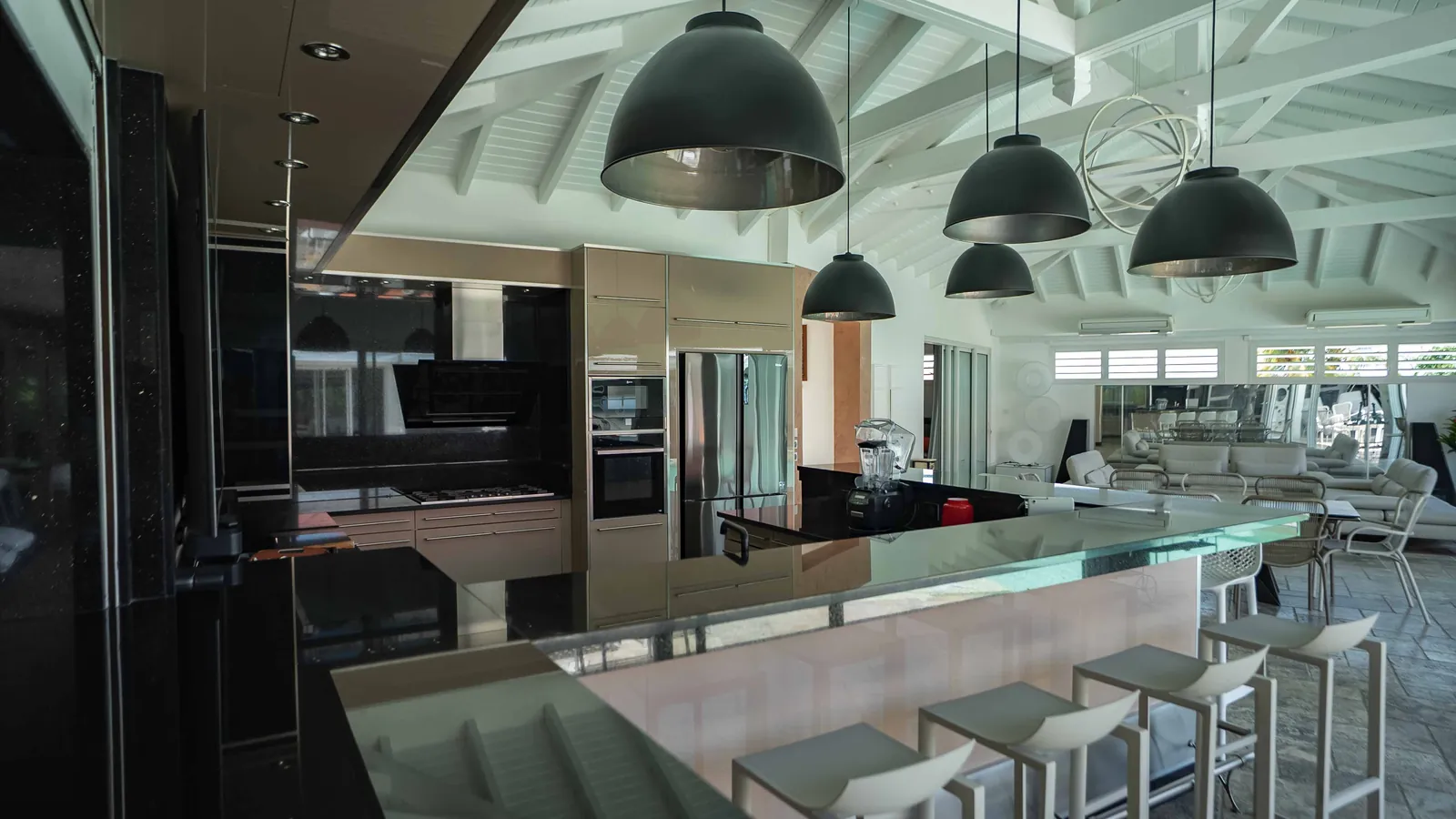La cuisine-bar côté piscine — suspensions noires, granit noir et bar de verre