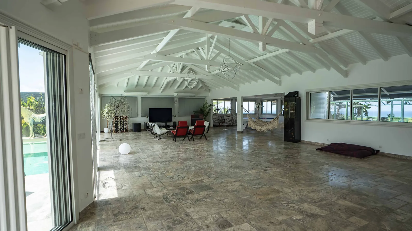 La grande salle, fauteuils et hamac, la piscine derrière les baies